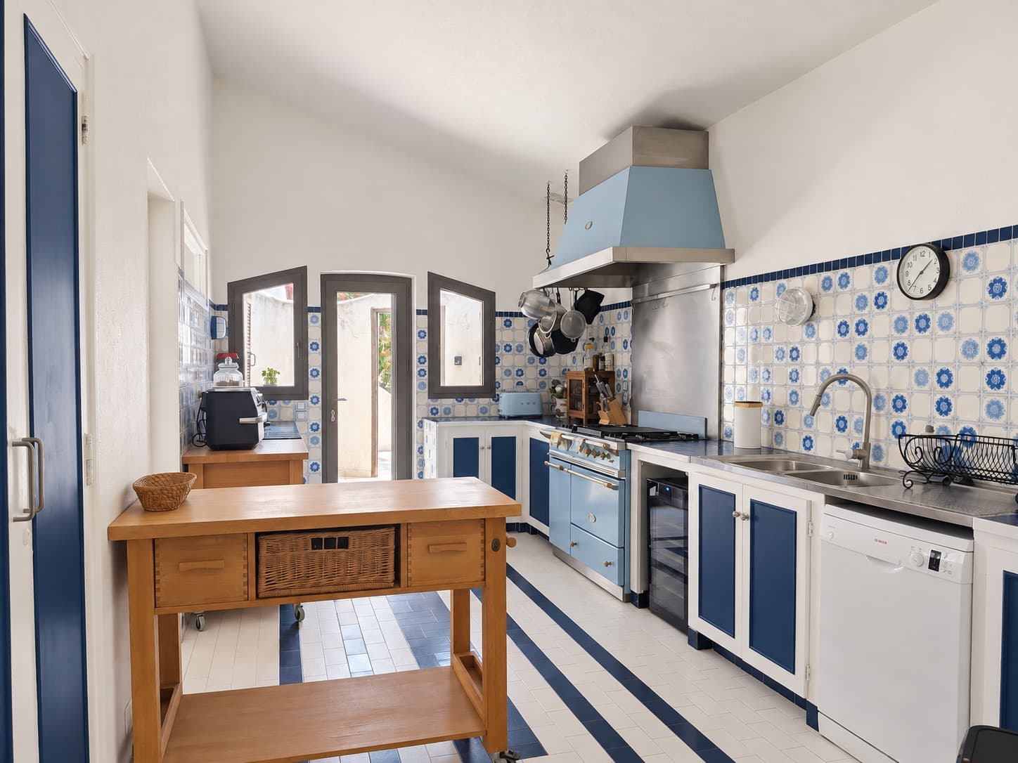 Cocina equipada, azulejos azules y blancos, isla de madera y puerta al exterior