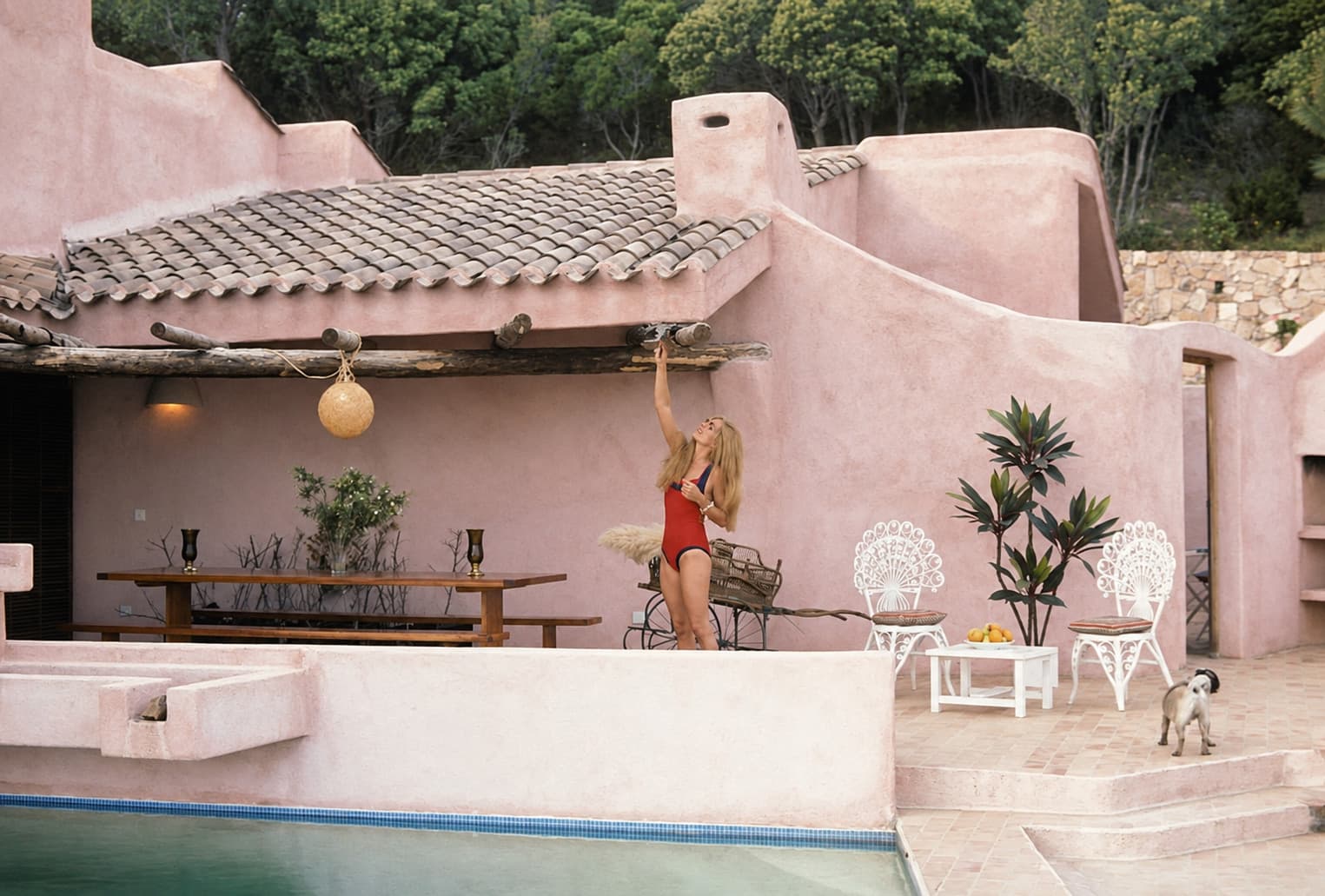 Dalida en bañador rojo delante de la casa de paredes rosas, la terraza cubierta y sus sillas de ratán