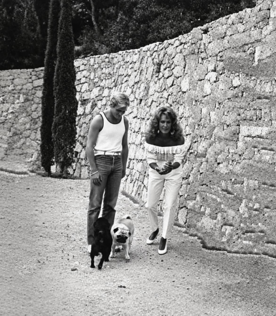 Dalida y un amigo jugando a la petanca junto a un muro de piedra, con sus perros