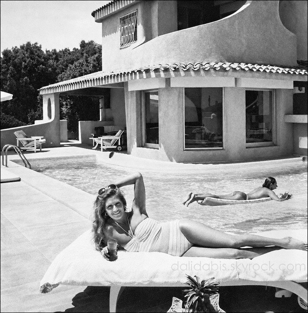 Dalida recostada en una tumbona junto a la piscina, con la casa detrás