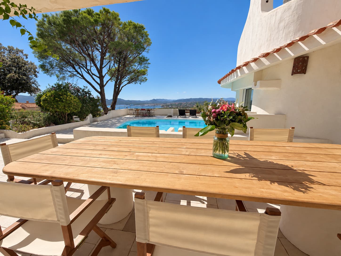 Teak table and canvas chairs facing the pool and the pines